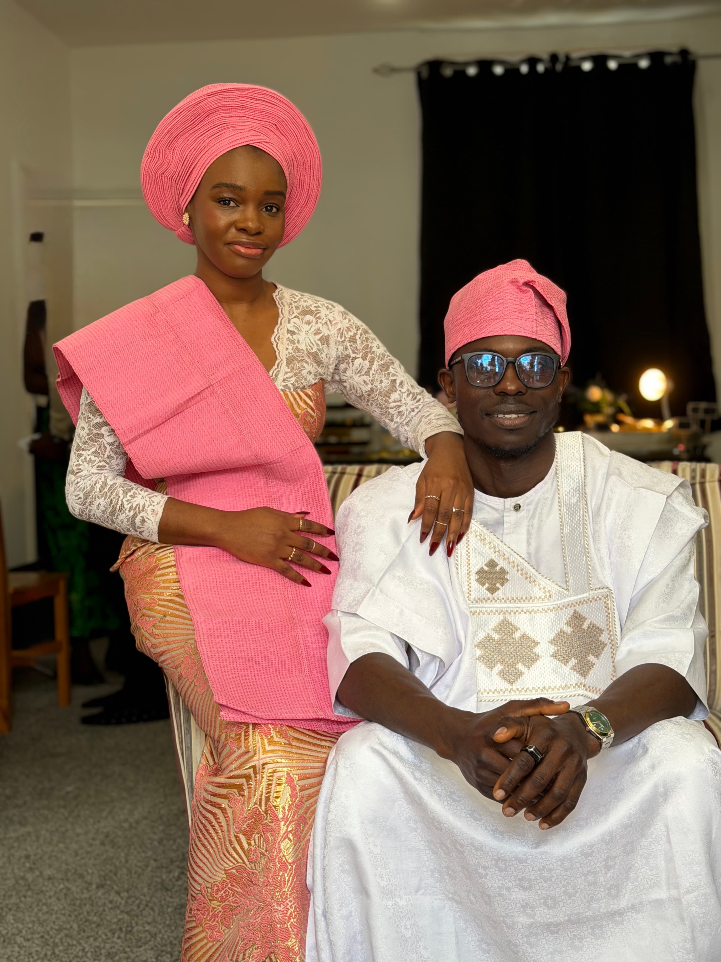Ola standing beside Ayo, both in traditional white and pink attire